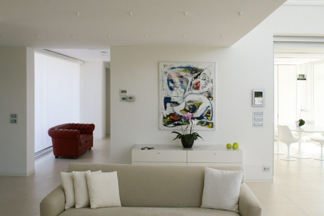Salotto moderno completamente bianco, divano in pelle rossa, dipinto moderno e tavolo tulip saarinen bianco