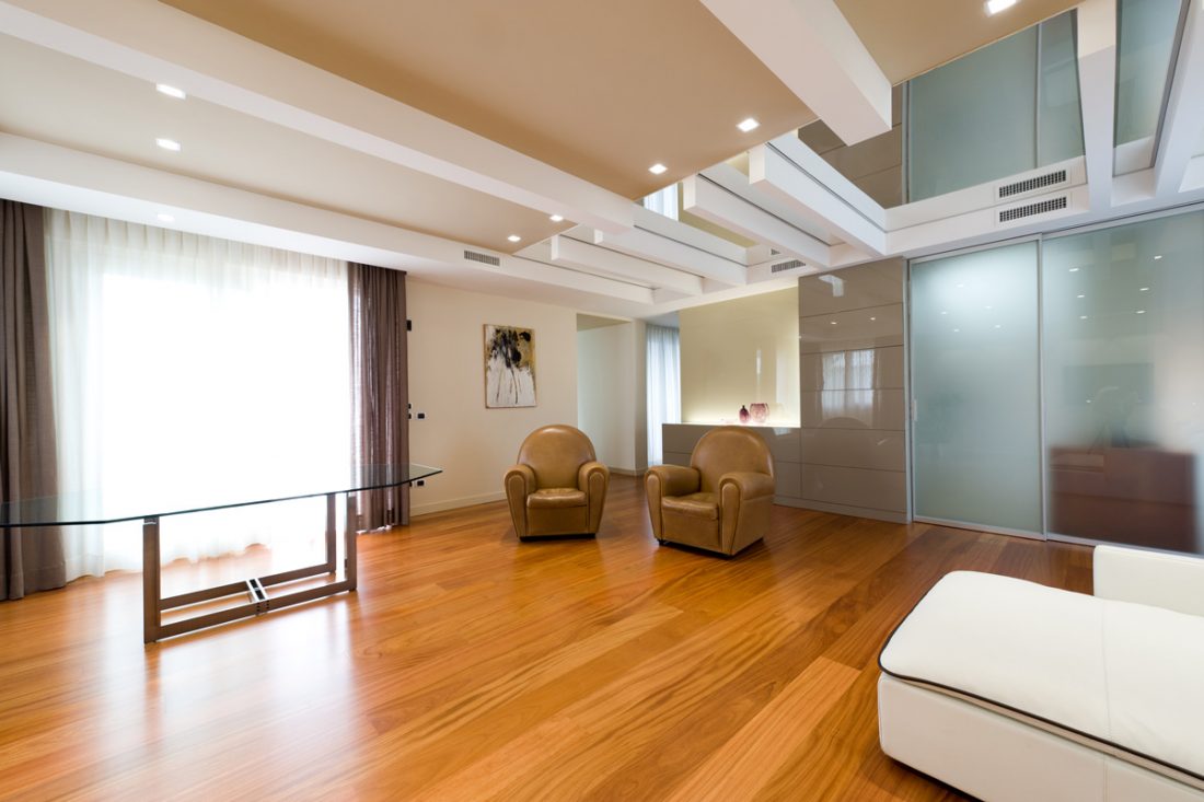 Uno spazioso soggiorno con parquet di legno, poltrone di pelle e tavolo con piano in vetro affacciato ad un'ampia vetrata