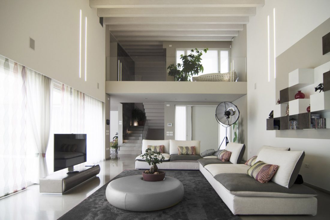 Salotto a doppia altezza con divano bianco e grigio, una lampada di design e un bonsai a decorare il coffee table