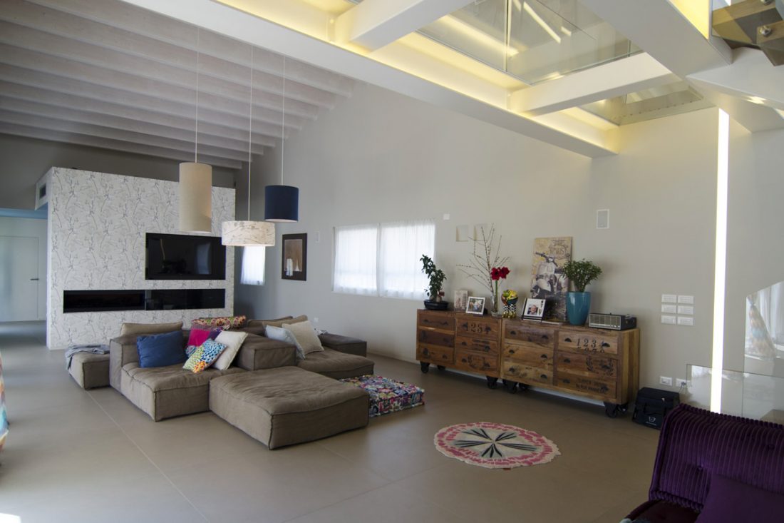 Interior design di un ampio soggiorno a doppia altezza con divano isola in tessuto grigio